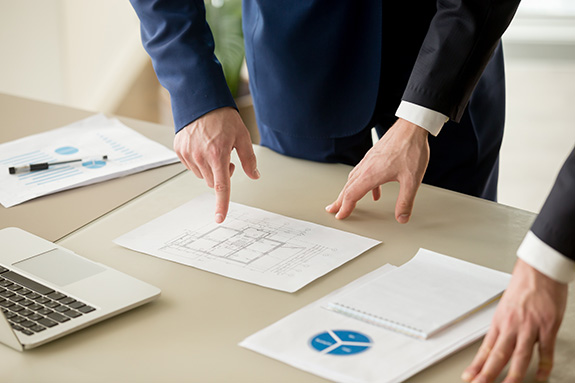 Close up view of businessmen discussing building plan, property value estimation, analyzing real estate market with infographic statistics, house evaluation, construction investment, home appraisal